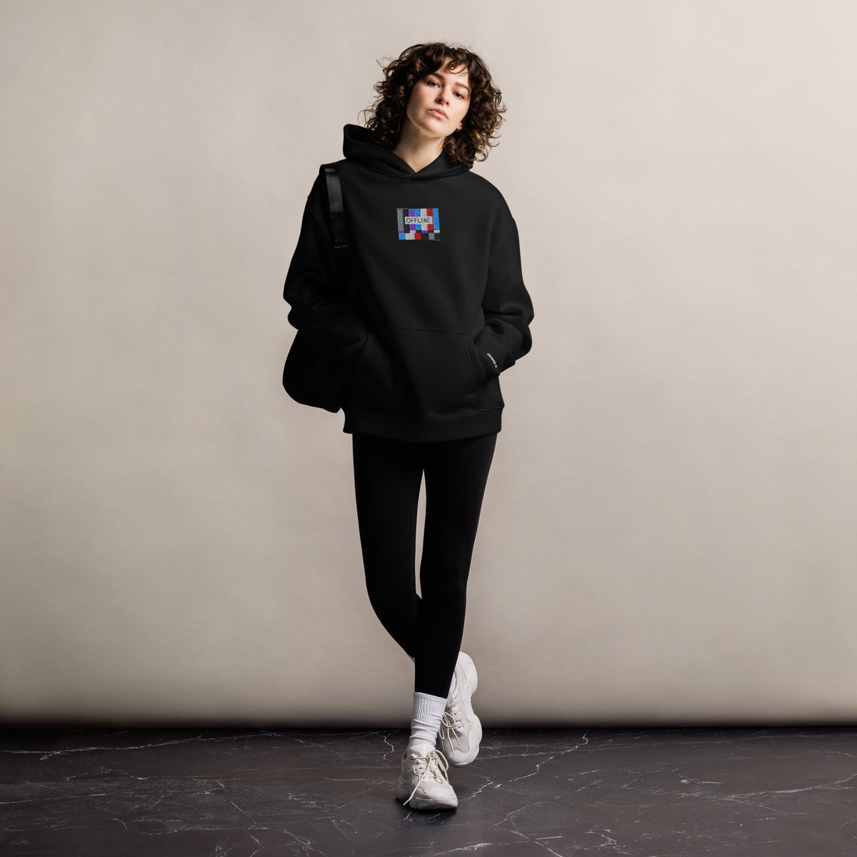 Offline unisex oversized hoodie in black, front view on a women's lifestyle model (Printful mockup)