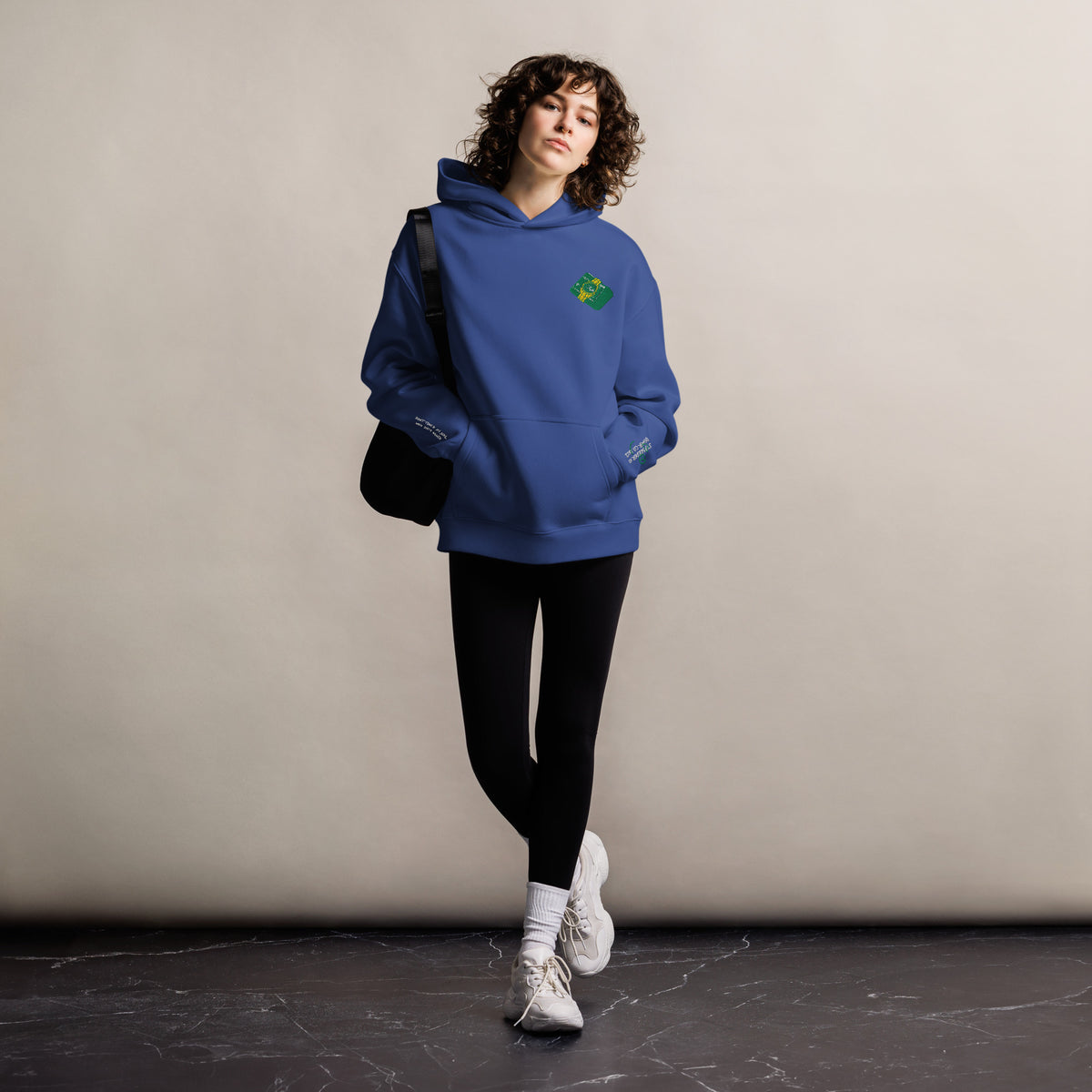 Mickey Money '22 unisex oversized hoodie in cobalt, front view on a women's lifestyle model (Printful mockup)